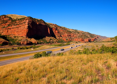 [Continuation of the segmented red rock dwarfing the vehicles on the interstate.]